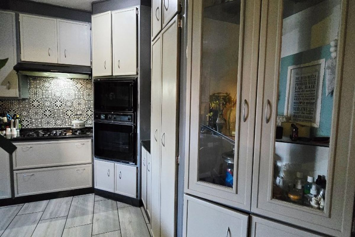 A well-maintained kitchen featuring built-in appliances, decorative tiled backsplash, and extensive cabinetry with glass-fronted display units.