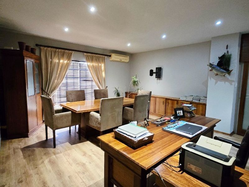 A spacious home office featuring laminate wood flooring, recessed downlighting, a wall-mounted air conditioning unit, and extensive built-in cabinetry.