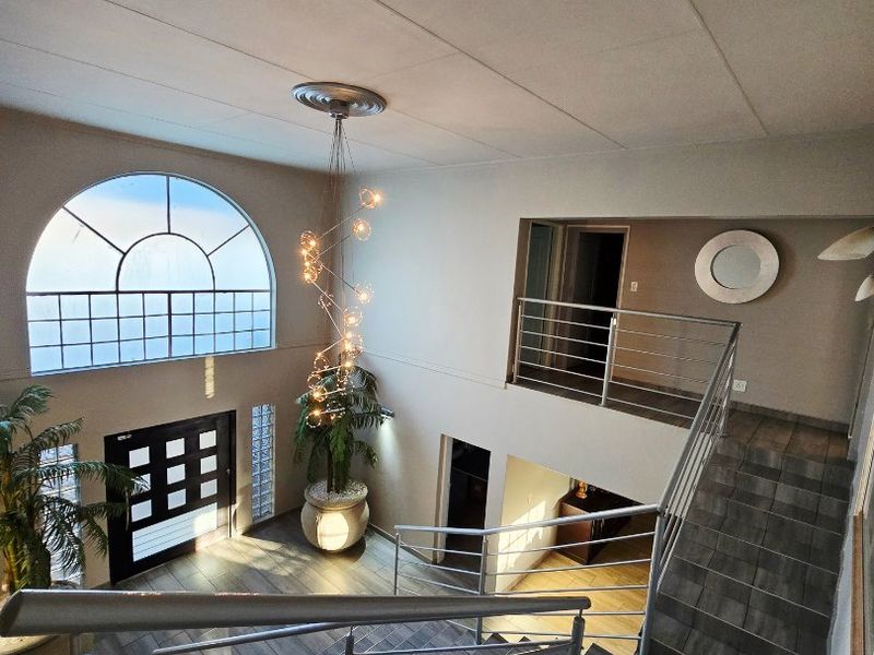 Spacious double-volume entrance hall featuring a modern staircase with stainless steel balustrades, large arched window, and contemporary pendant lighting.