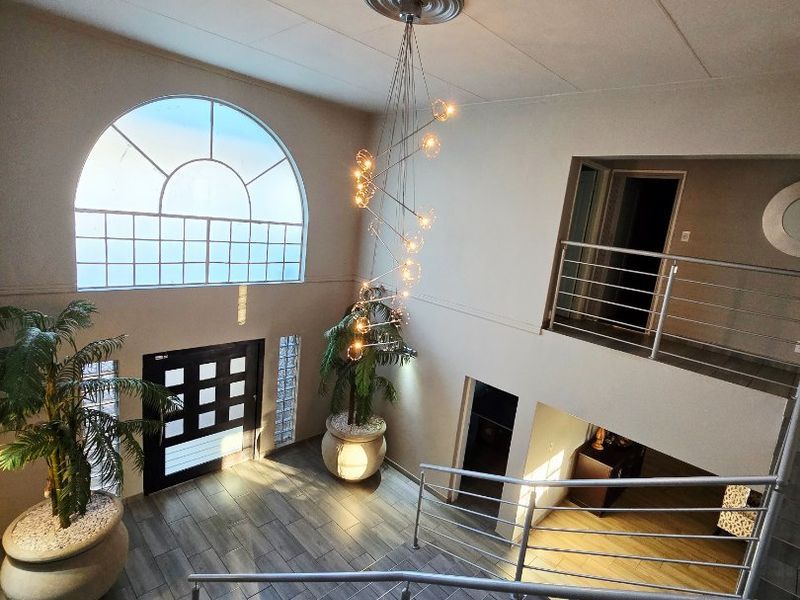Spacious double-volume entrance hall featuring a grand staircase, modern metal railings, large arched window, and elegant suspended feature lighting.