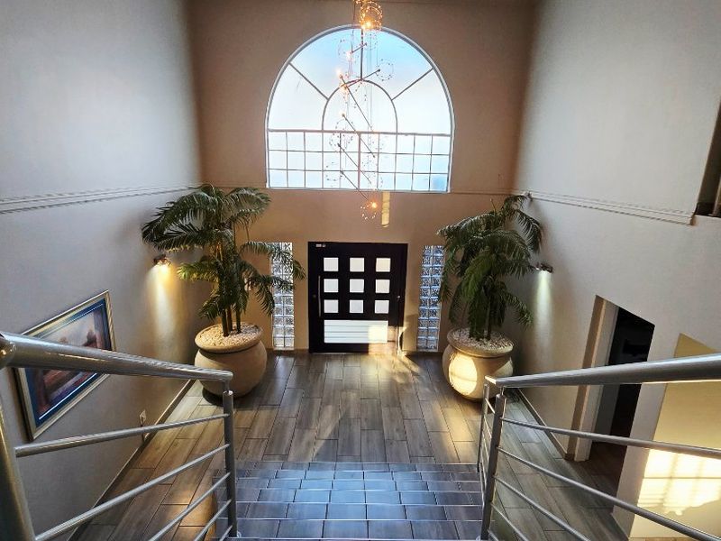 Spacious entrance foyer featuring a grand staircase with metal balustrades, an arched window, and modern tiled flooring, creating a bright and welcoming atmosphere.