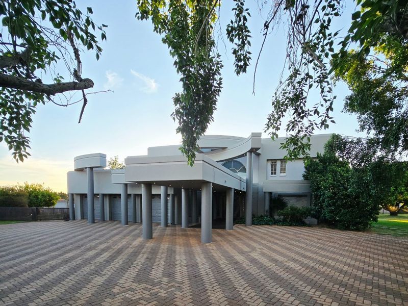 Front elevation of a modern farm-style residence featuring a large paved driveway, prominent covered portico with structural columns, and integrated multi-car garage.