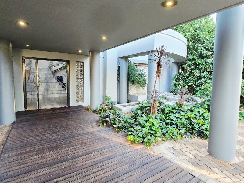 A modern covered entrance featuring timber decking, recessed lighting, and a glass block feature wall leading to the main building access.