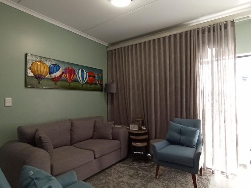 A comfortable living room featuring soft green walls, neutral flooring, and a large sliding glass door with floor-to-ceiling curtains providing natural light.