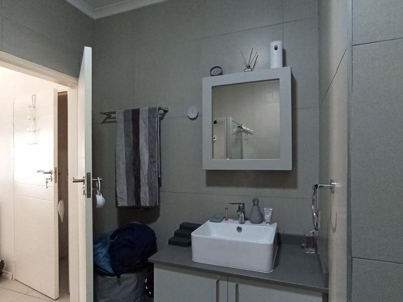 A functional bathroom featuring a modern vessel sink, vanity cabinet, wall-mounted mirror cabinet, and neutral wall tiling.