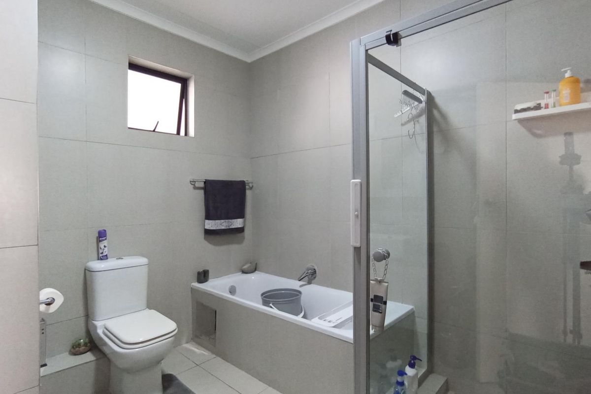 A functional bathroom featuring a built-in bathtub, a separate glass-enclosed shower, and neutral wall tiling.