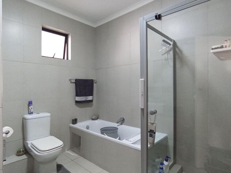 A functional bathroom featuring a built-in bathtub, a separate glass-enclosed shower, and neutral wall tiling.