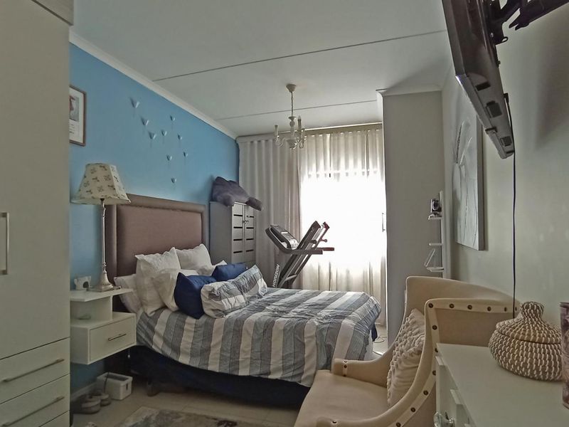 A functional bedroom featuring a built-in wardrobe, neutral wall finishes, and natural light through window curtains.
