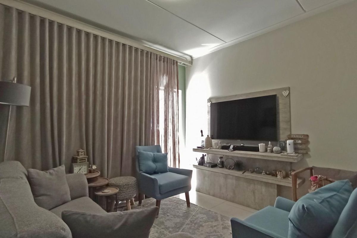 A comfortable living room featuring a built-in media console, tiled flooring, and floor-to-ceiling curtains providing natural light control.