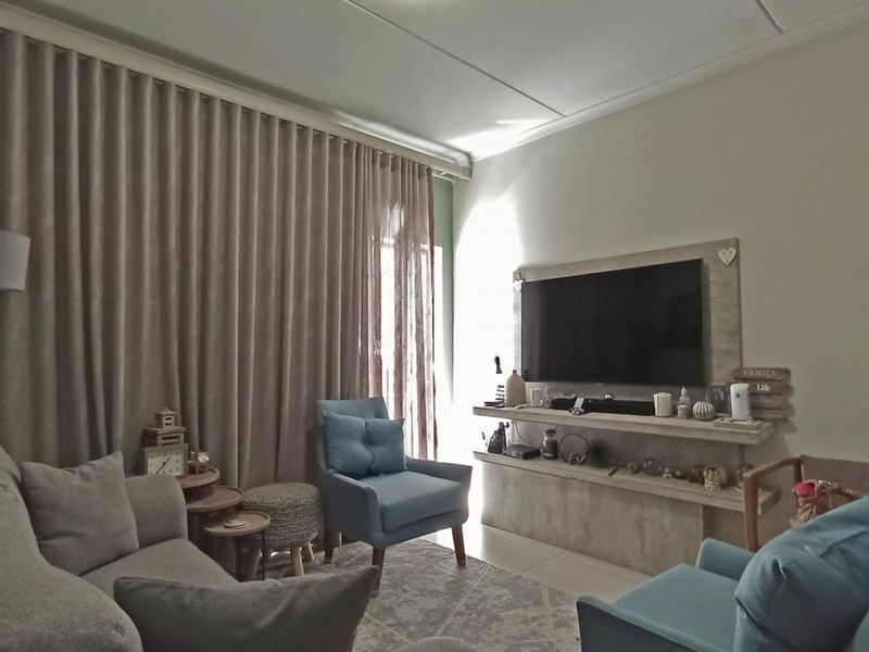 A comfortable living room featuring a built-in media console, tiled flooring, and floor-to-ceiling curtains providing natural light control.