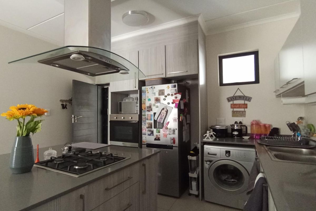 Modern kitchen featuring stone countertops, a gas hob with extractor fan, built-in oven, and integrated laundry facilities with ample cabinetry.
