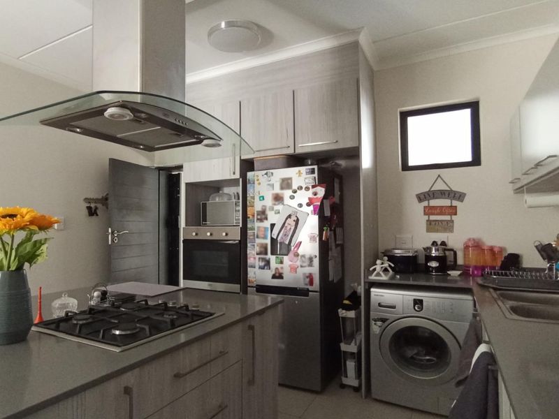 Modern kitchen featuring stone countertops, a gas hob with extractor fan, built-in oven, and integrated laundry facilities with ample cabinetry.