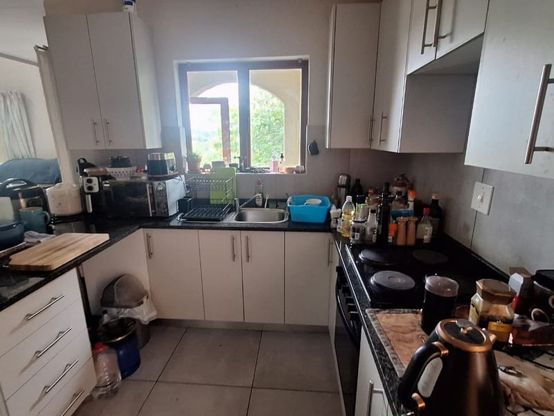 A functional kitchen featuring built-in cabinetry, granite countertops, an electric hob, and an integrated oven, with tiled flooring and a window overlooking the exterior.