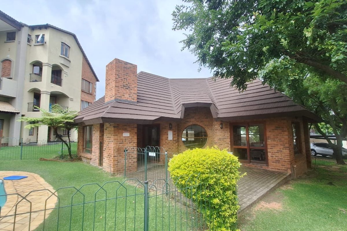 Exterior view of a brick-faced building featuring a tiled roof, chimney, and circular window, set within a landscaped garden area with a swimming pool.