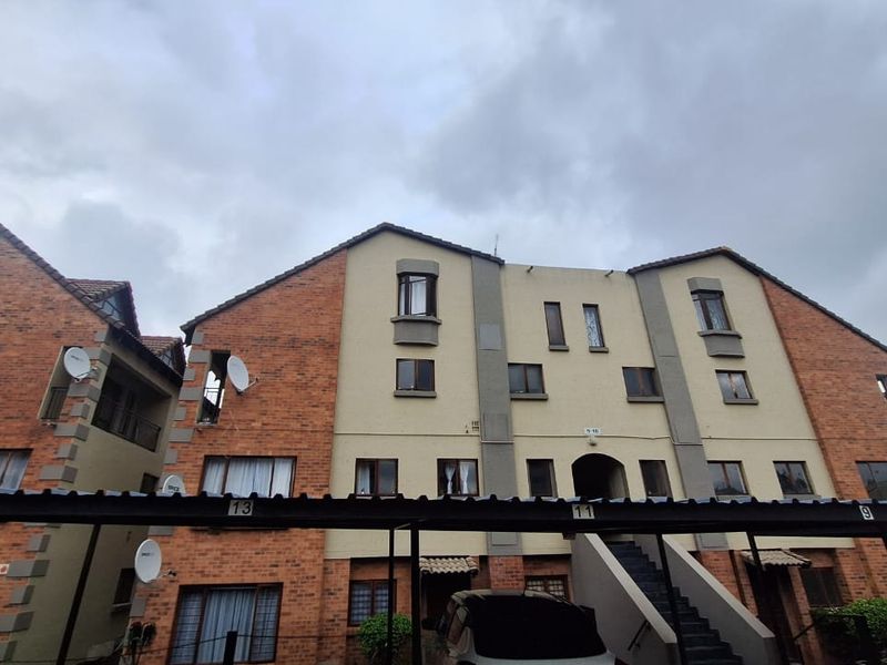 Exterior view of a multi-story apartment complex featuring brick and plaster facade, tiled roofing, and an integrated carport structure.
