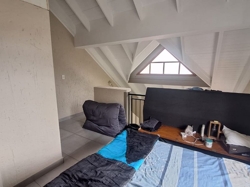 Loft-style bedroom featuring a vaulted ceiling with exposed rafters, tiled flooring, and a unique triangular window.