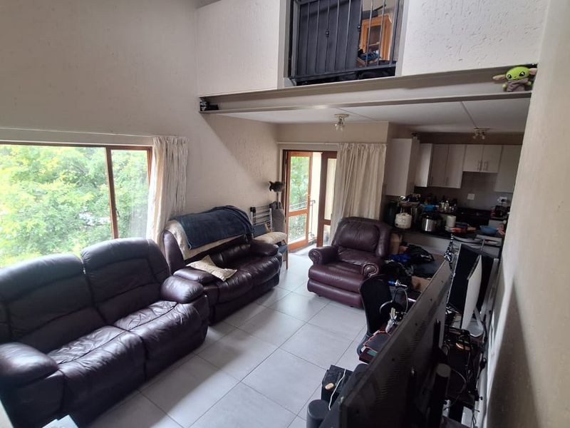 Open-plan living area featuring tiled floors, an exposed steel beam, and a mezzanine level, with direct access to an outdoor balcony.