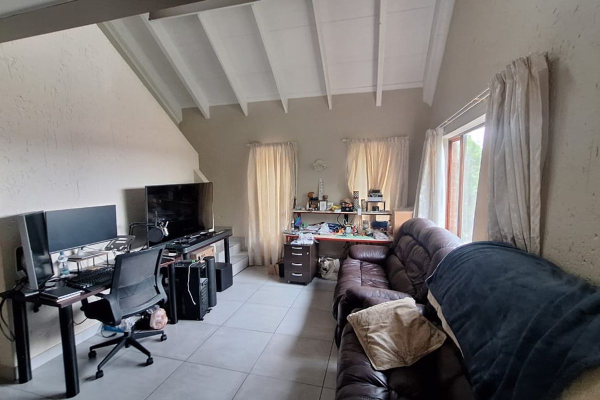 Spacious living area featuring a high vaulted ceiling with exposed rafters, large windows for natural light, and neutral tiled flooring throughout.