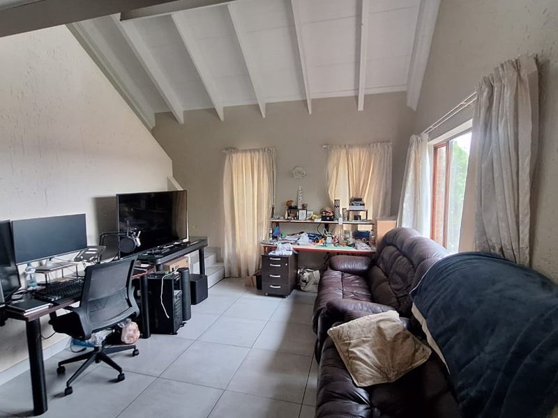 Spacious living area featuring a high vaulted ceiling with exposed rafters, large windows for natural light, and neutral tiled flooring throughout.