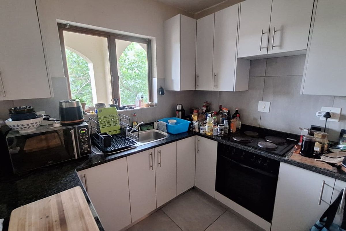 A functional kitchen featuring white cabinetry, granite countertops, a built-in oven, and an electric hob, with tiled splashbacks and flooring.