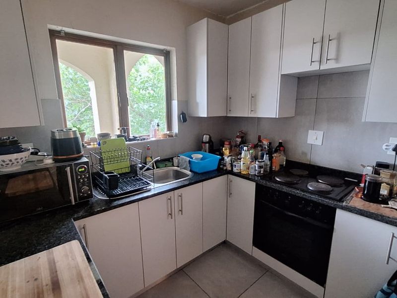 A functional kitchen featuring white cabinetry, granite countertops, a built-in oven, and an electric hob, with tiled splashbacks and flooring.
