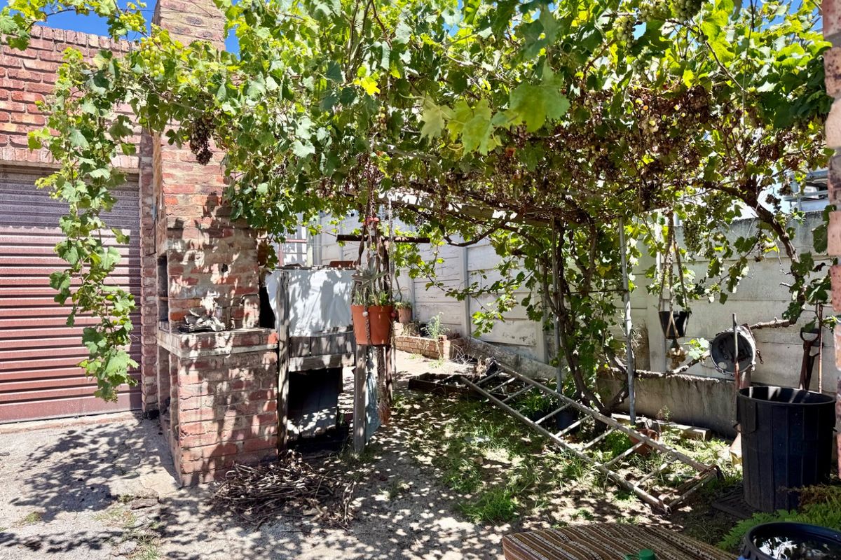 Rear outdoor area featuring a brick fireplace and established grapevine trellis, offering potential for a charming garden entertainment space.