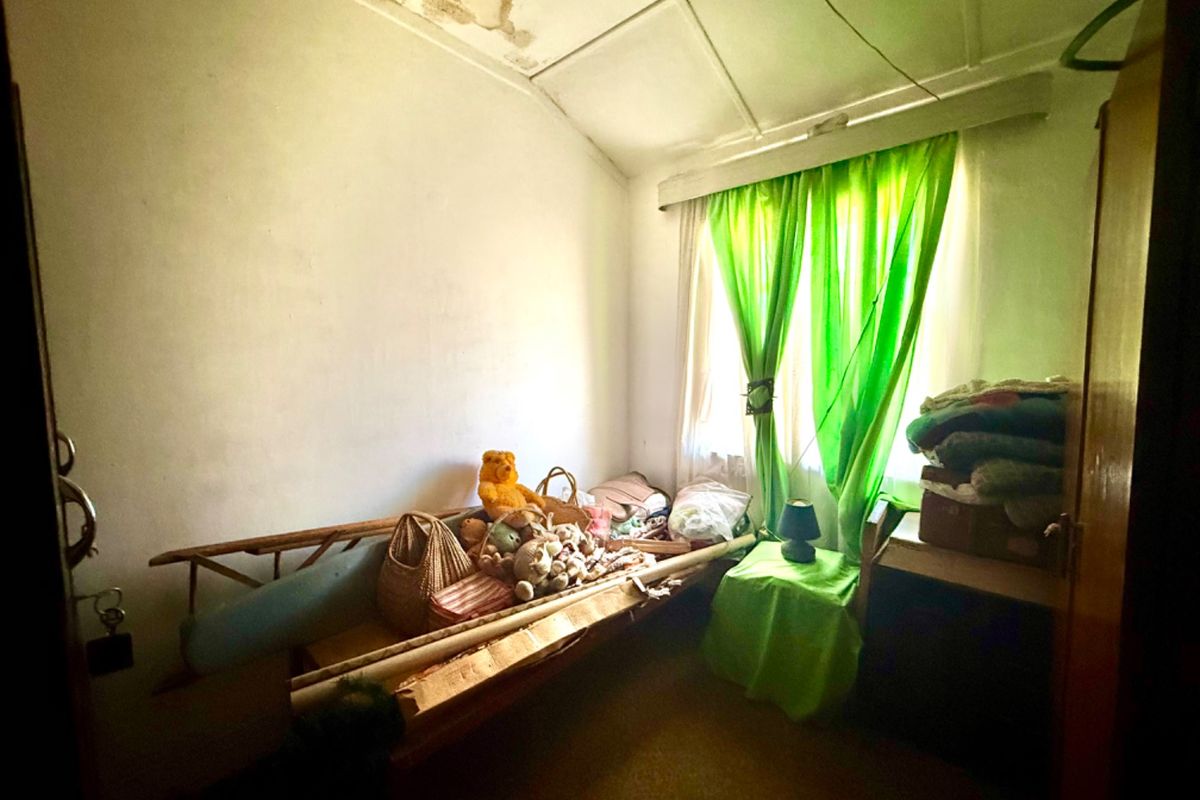 A bedroom space featuring a window and a tiled ceiling, currently showing signs of water damage and requiring maintenance and renovation.