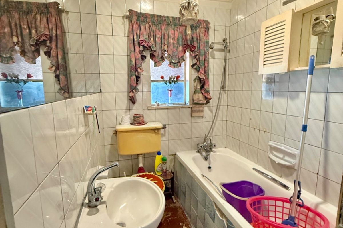 A dated bathroom featuring a pedestal basin, bathtub with shower mixer, and timber ceiling. The space requires modernization of finishes and fixtures.