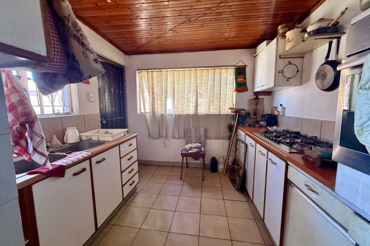 A dated kitchen featuring built-in cabinetry, a gas hob, and an integrated oven, finished with tiled flooring and a timber ceiling.