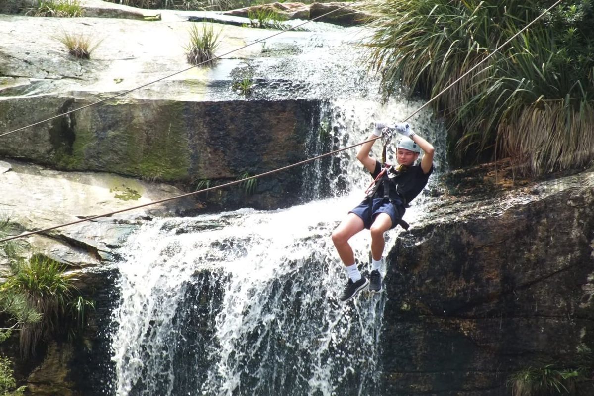 Outdoor adventure sports facility featuring a zip line course set against a natural waterfall landscape.