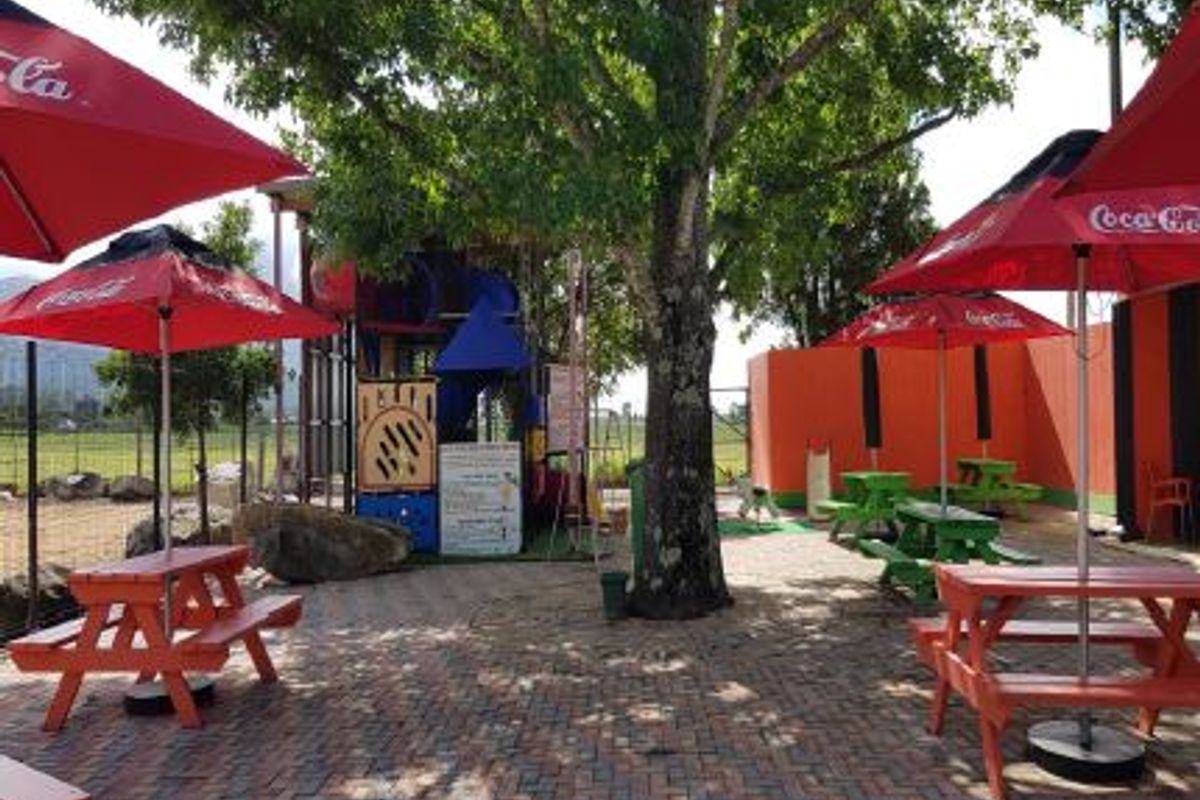 Outdoor commercial patio area featuring paved flooring, a children's play structure, and shaded seating areas under large umbrellas.
