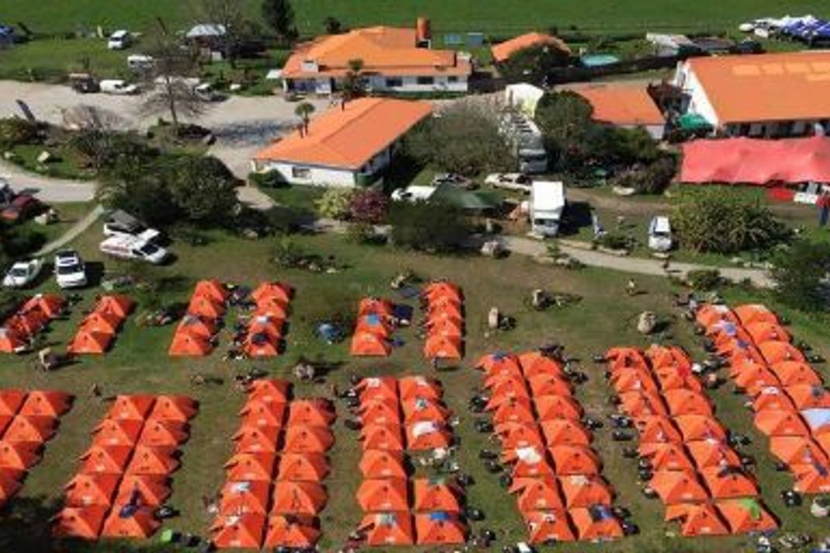 Aerial view of a commercial property complex featuring multiple buildings, paved access roads, and extensive outdoor grounds currently utilized for event camping.