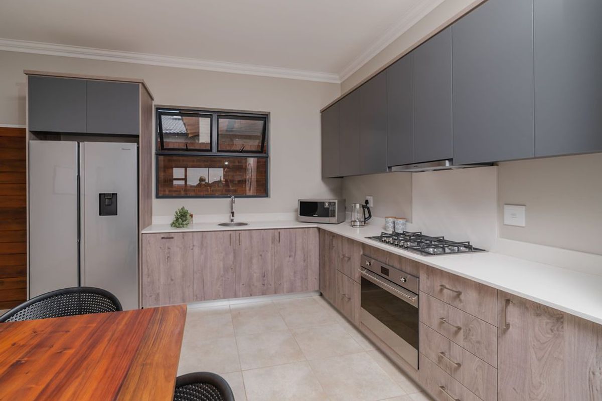 Modern kitchen featuring two-tone cabinetry, stone countertops, gas hob, built-in oven, extractor fan, and tiled flooring.