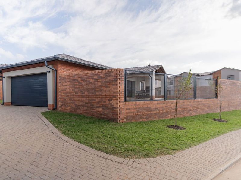 A well-maintained townhouse exterior featuring a brick boundary wall with metal fencing, a paved driveway, and a modern sectional garage door.