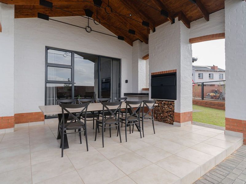 Covered patio featuring a built-in braai, exposed timber ceiling, and tiled flooring, providing a seamless transition to the outdoor garden area.