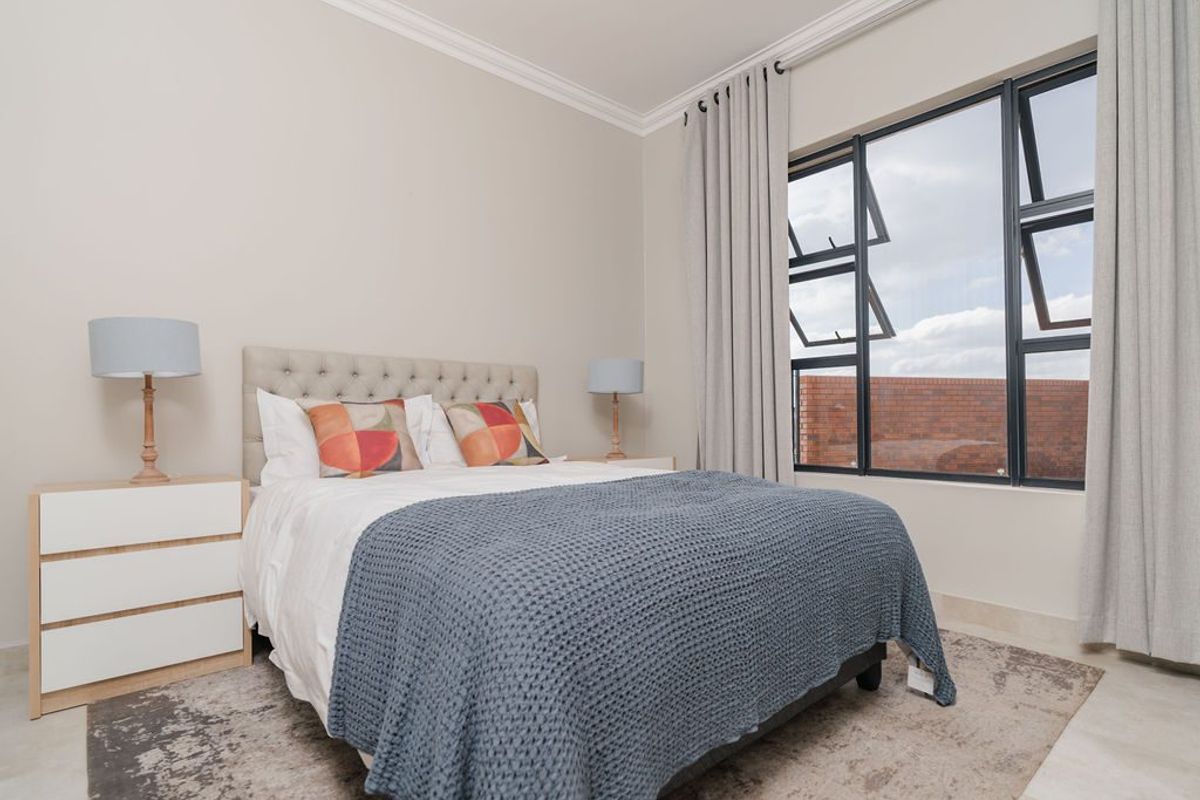 A well-maintained bedroom featuring neutral wall tones, tiled flooring, decorative cornicing, and large aluminium-framed windows allowing for natural light.