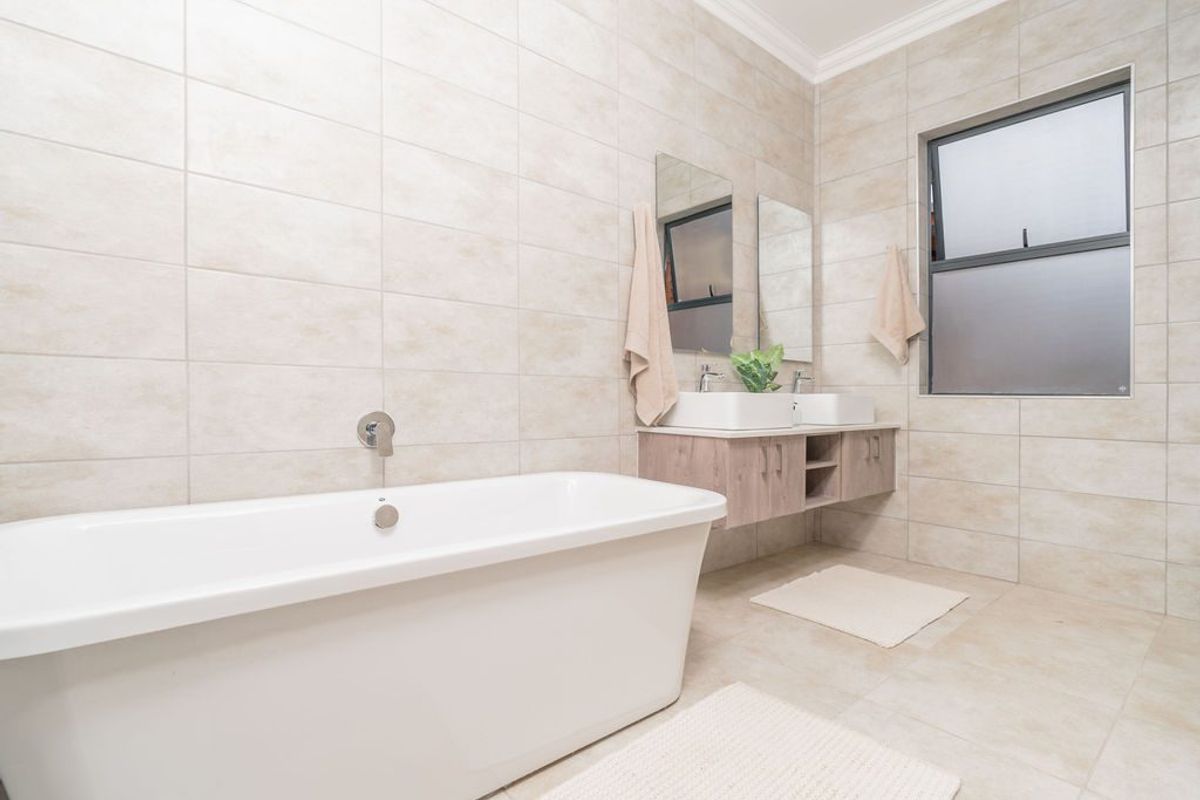 Modern bathroom featuring a sleek freestanding bathtub, wall-mounted double vanity with vessel sinks, and neutral floor-to-ceiling tiling.