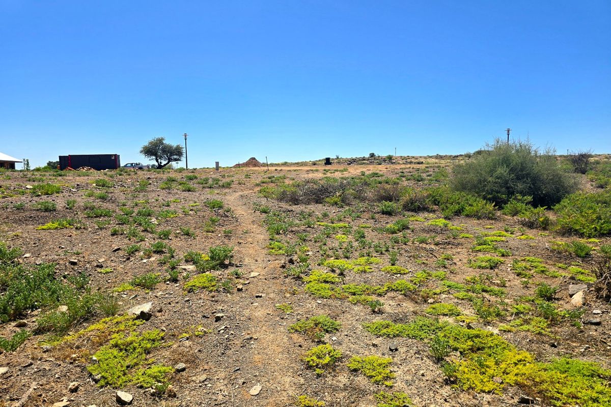 A view of a vacant residential plot featuring natural vegetation, rocky terrain, and clear blue skies.