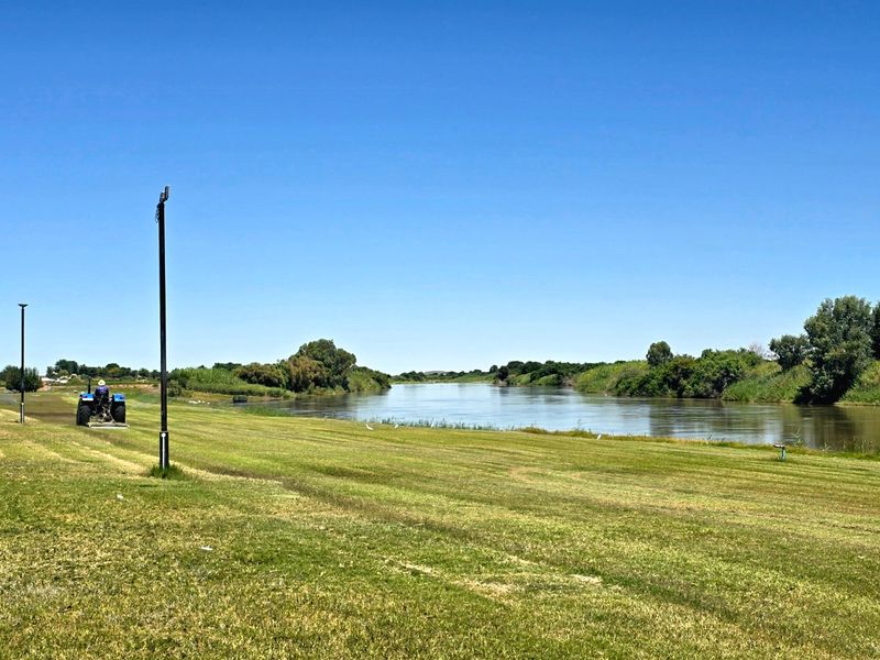 A scenic view of the river frontage featuring expansive green lawns and natural vegetation along the water's edge.