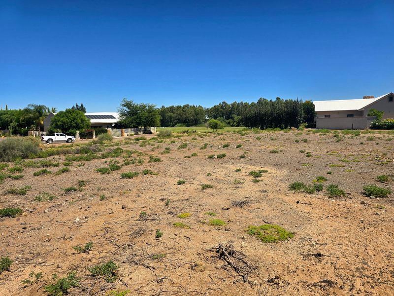 A view of a vacant residential plot of land with natural ground cover, situated in a developed neighborhood setting.