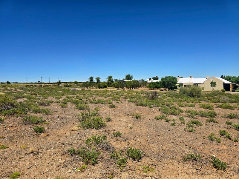 A wide-angle view of a vacant residential plot featuring natural scrub vegetation and open space, with neighboring properties visible in the distance.