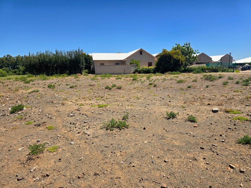 A view of an undeveloped residential plot of land with a boundary wall and neighboring properties in the background.
