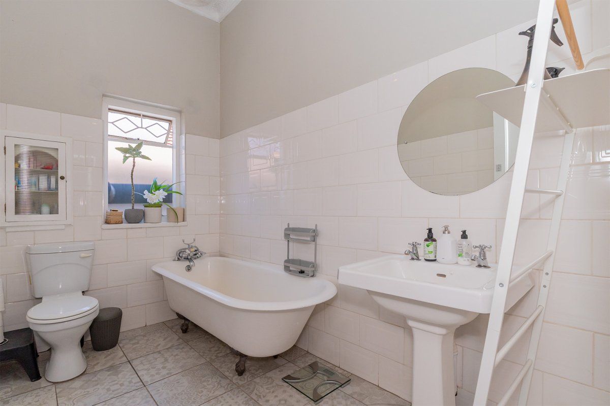 A classic bathroom featuring a vintage-style clawfoot bathtub, pedestal basin, and neutral wall tiling with patterned floor tiles.