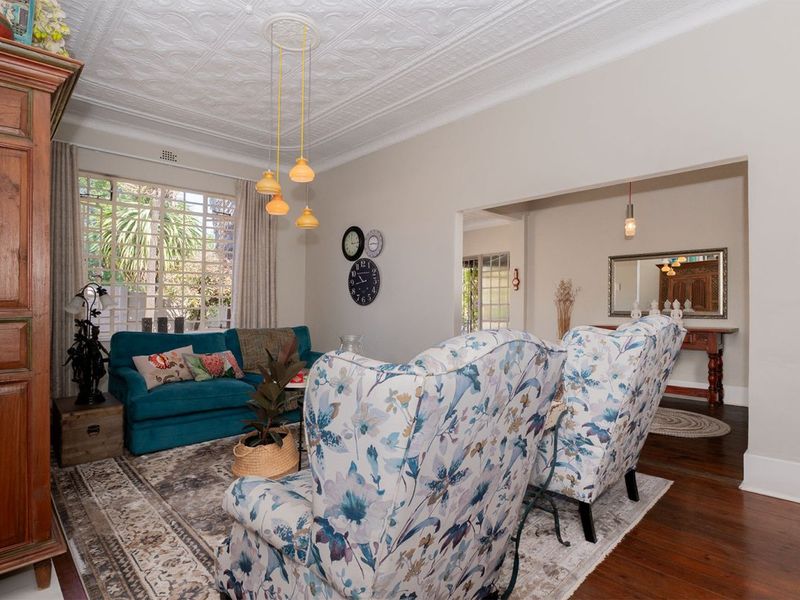 A character-filled living room featuring a decorative pressed metal ceiling, original timber flooring, and large windows that provide ample natural light.