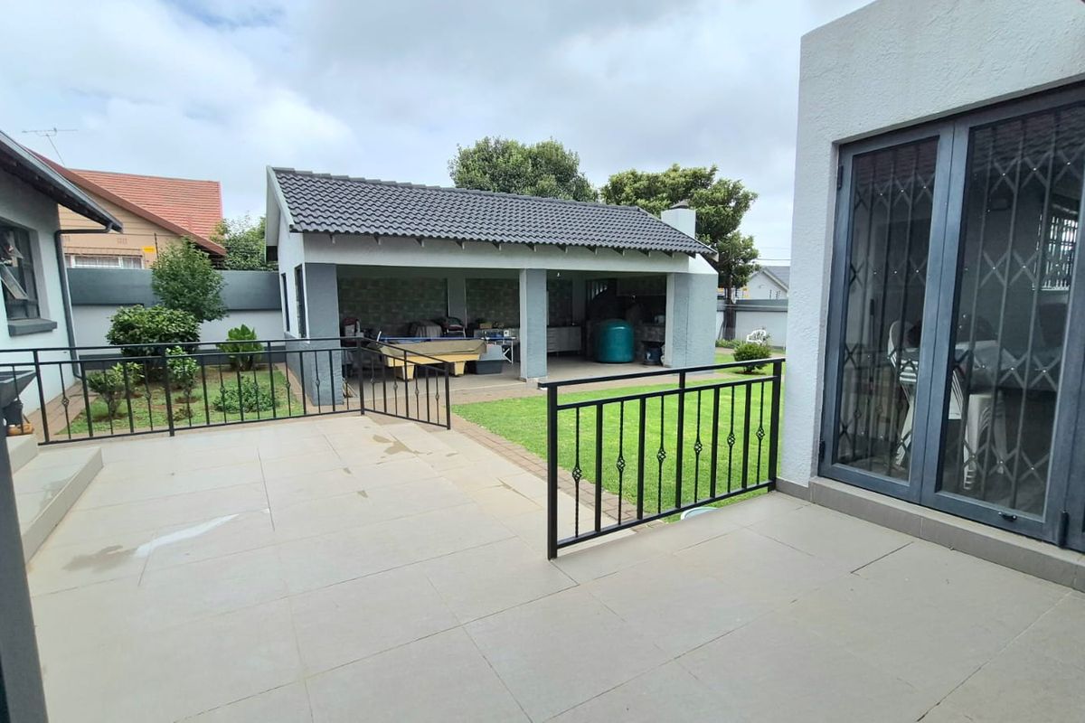Rear view of the property featuring a tiled patio, a manicured lawn, and a covered outdoor entertainment area with a tiled roof.