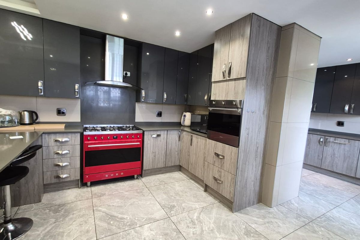 Modern kitchen featuring high-gloss and wood-grain cabinetry, stone countertops, tiled flooring, and a prominent red Smeg gas stove with integrated oven.
