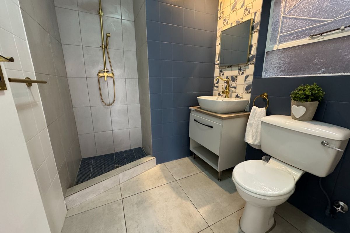 Modern bathroom featuring a walk-in shower with brass fixtures, a vanity unit with a vessel sink, and stylish blue and patterned wall tiling.
