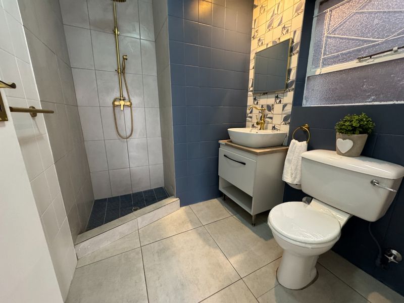 Modern bathroom featuring a walk-in shower with brass fixtures, a vanity unit with a vessel sink, and stylish blue and patterned wall tiling.