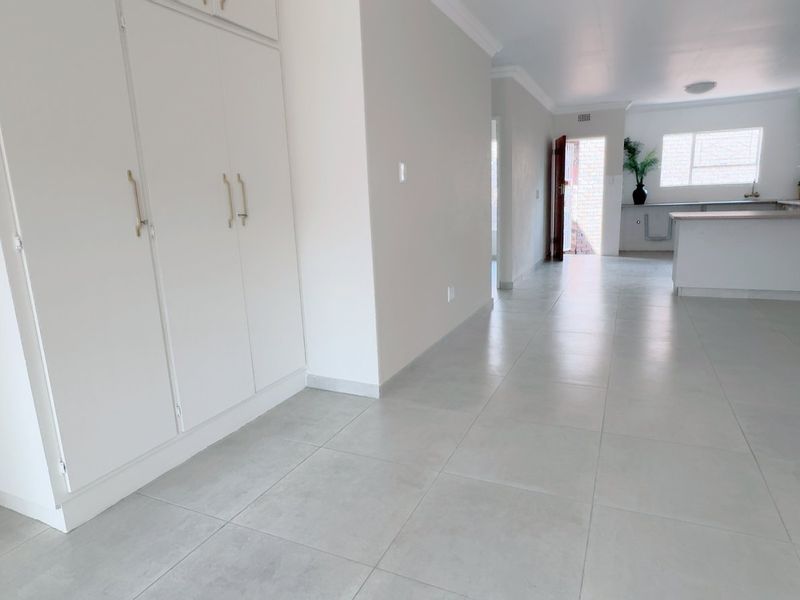 Spacious open-plan living area featuring neutral tiled flooring, built-in storage cabinetry, and a modern kitchen with a functional island layout.