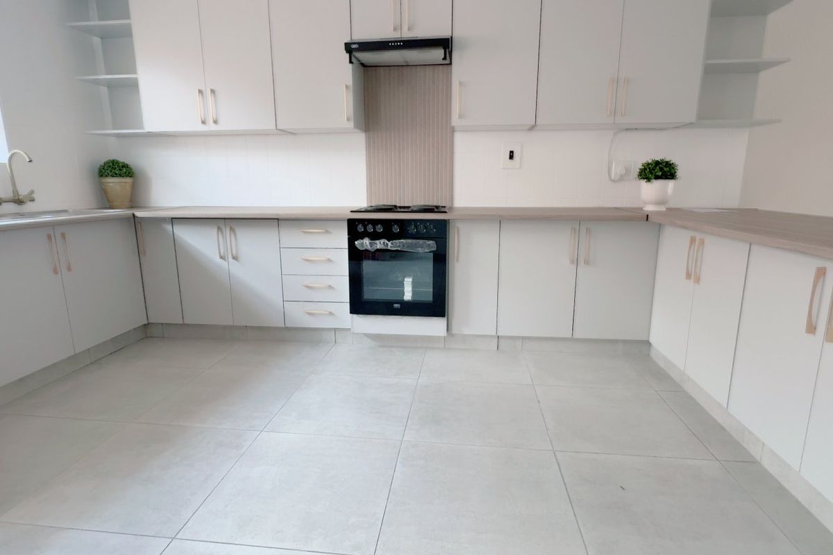 A clean, modern kitchen featuring light-toned cabinetry, laminate countertops, built-in oven with extractor fan, and neutral tiled flooring.